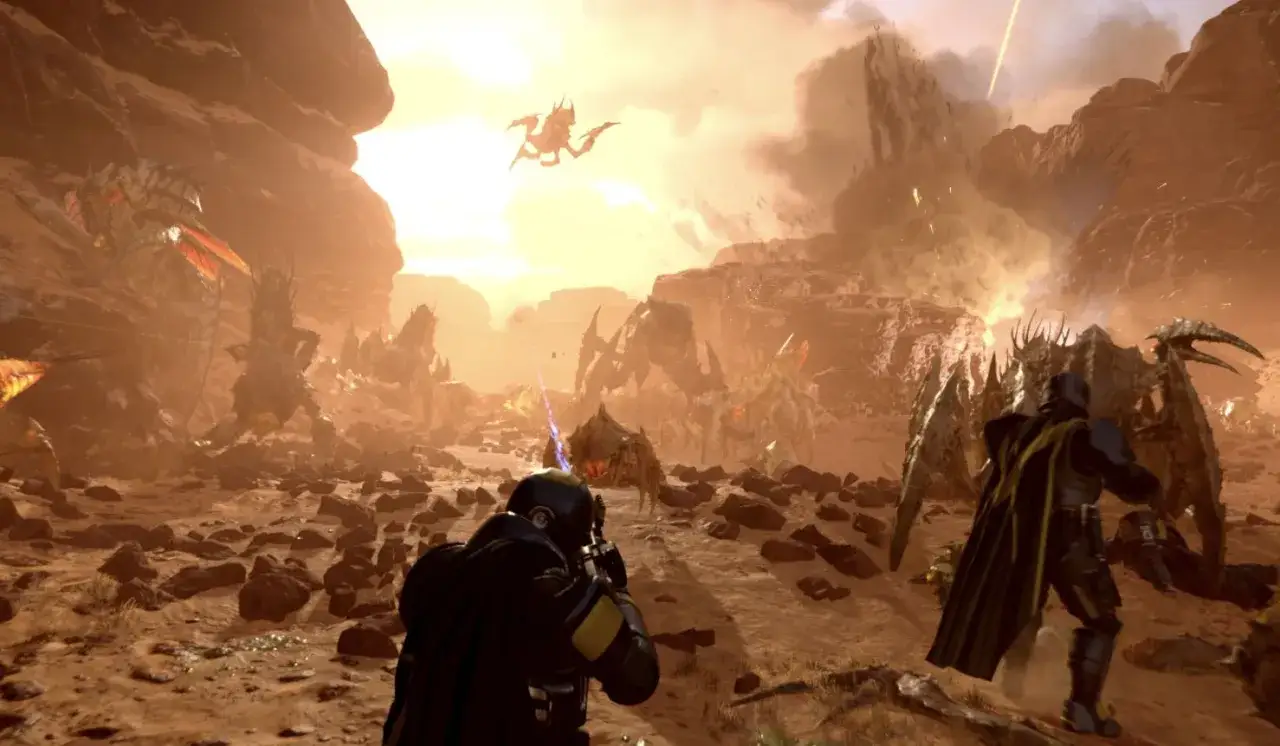 Helldivers 2: żołnierze walczą z rojem potworów na pustynnej planecie. W tle latający przeciwnik i wybuchy.
